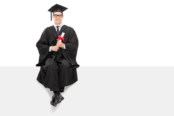 Graduado universitario sentado en cartelera en blanco — Foto de Stock