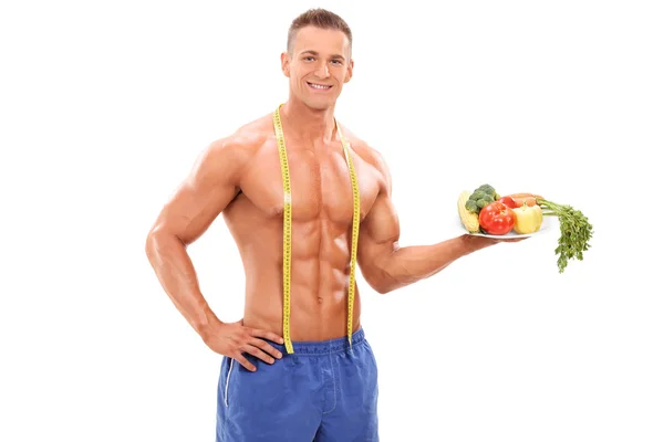 Shirtless athlete holding plate with vegetables — Stock Photo, Image