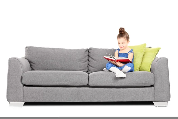 Lilla flickan läsa bok på soffa — Stockfoto