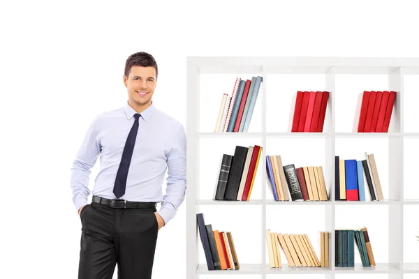 Молодой бизнесмен, опирающийся на книжную полку — стоковое фото