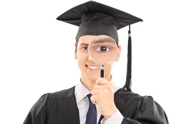 Graduate looking through magnifying glass — Stock Photo, Image