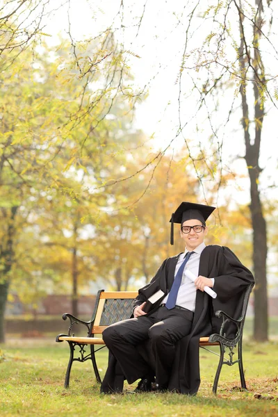 College student holding diploma en een boek in park — Stockfoto