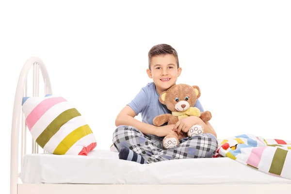 Menino na cama abraçando ursinho de pelúcia — Fotografia de Stock