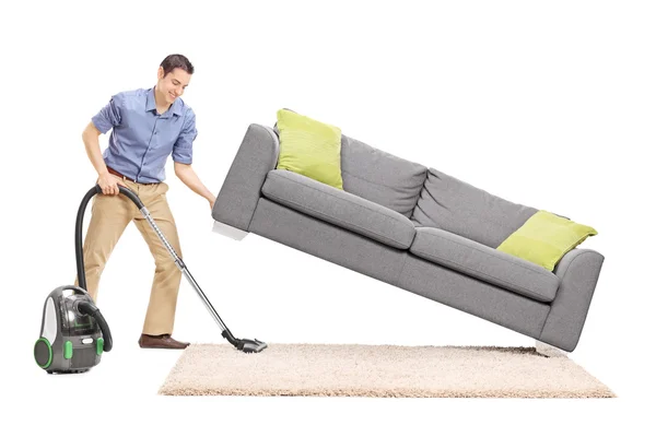 Mężczyzna podnoszenia sofę i odkurzanie spodem — Zdjęcie stockowe