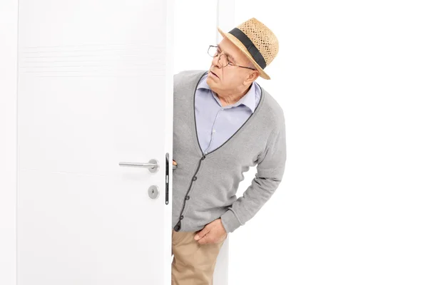 Senior looking at something behind a door — Stock Photo, Image