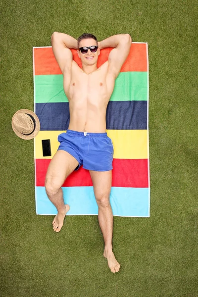 Hombre guapo acostado en una toalla y tomando el sol — Foto de Stock