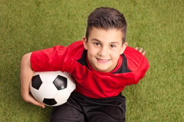 Çimenlerin üzerinde oturan genç futbol oyuncu