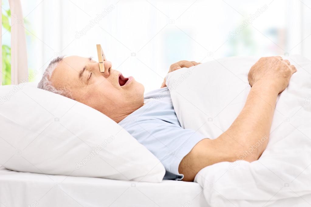 Senior man sleeping with a clothespin on nose