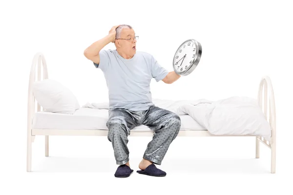 Zszokowany mężczyzna na łóżku trzymając zegar — Zdjęcie stockowe