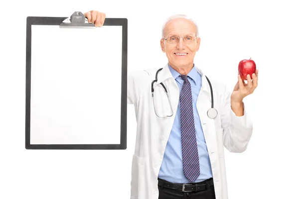 Mature doctor holding apple and a clipboard — Stock Photo, Image