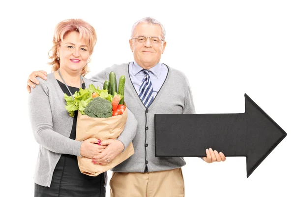 Mature couple holding groceries and an arrow — Stock Photo, Image