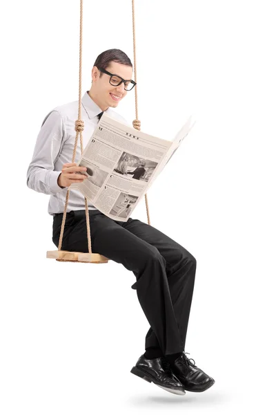 Businessman reading newspaper seated on a swing — Stock Photo, Image