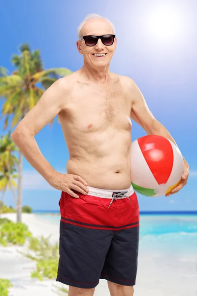 Старший чоловік тримає пляжний м'яч на пляжі — стокове фото