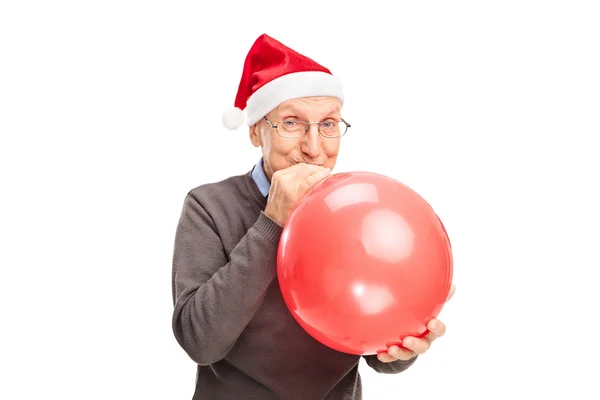 Senior with Santa hat blowing up a balloon — Stockfoto