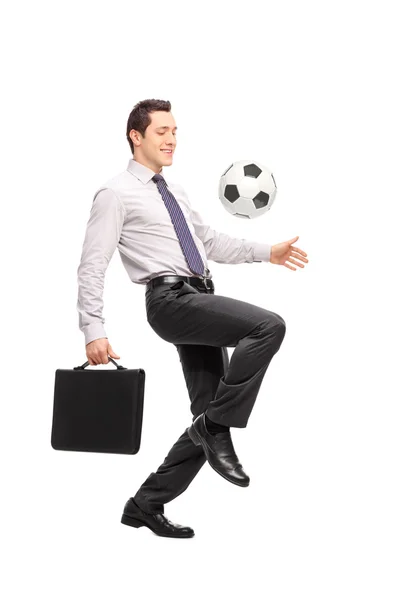 Businessman holding a briefcase and juggling a football — Stockfoto