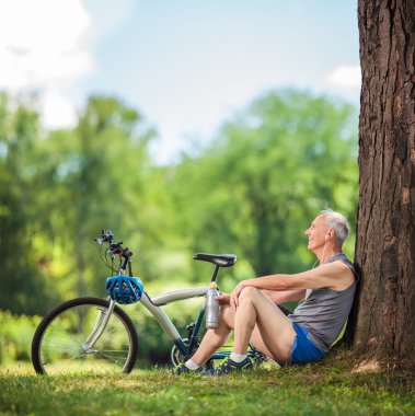 Senior cyclist sitting by a tree in park 