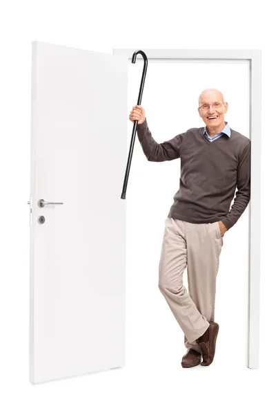 Fröhlicher Senior zeigt seinen Stock und lehnt eine Tür — Stockfoto