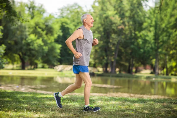 Active senior jogging in a park and listening to music — Stockfoto