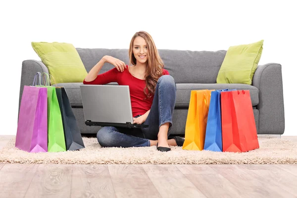 Jovem segurando um laptop sentado na frente de um sofá — Fotografia de Stock