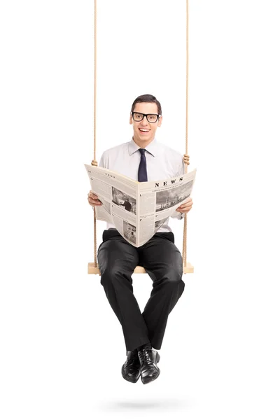 Man reading a newspaper seated on a swing — 图库照片