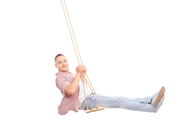 Delighted young man swinging on a wooden swing — Stockfoto