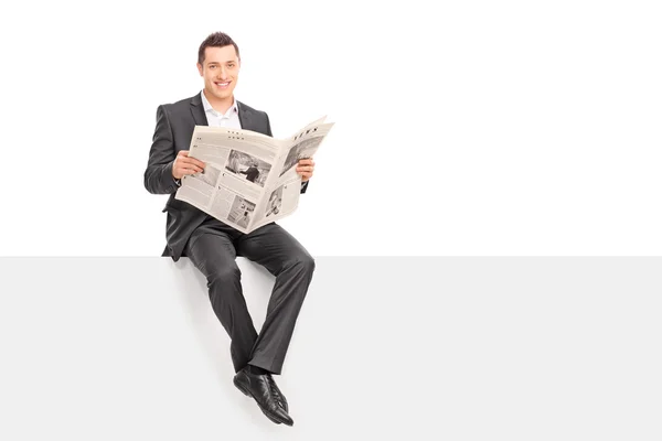 Businessman holding a newspaper seated on a panel — Stockfoto