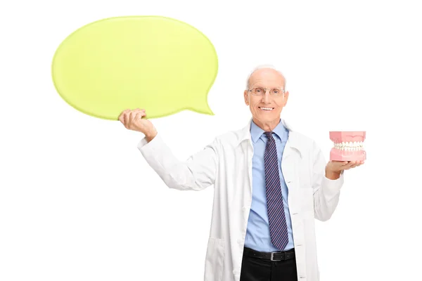 Mature dentist holding denture and a speech bubble — Zdjęcie stockowe