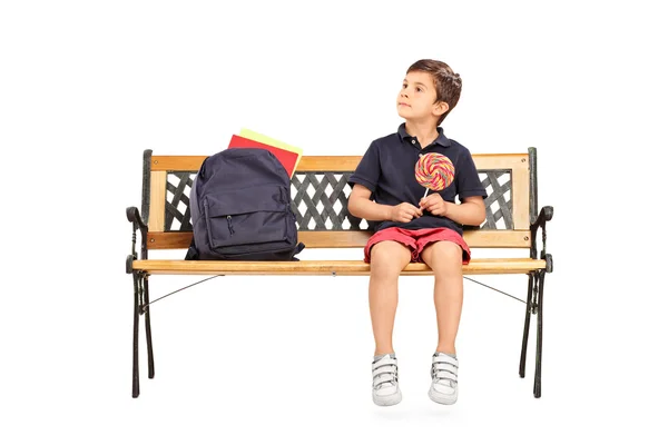 Schoolboy sitting on a bench and holding lollipop — Stock Photo, Image