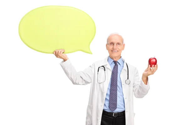 Mature doctor holding apple and speech bubble — Stock Photo, Image
