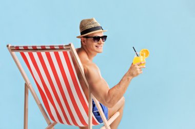 Bir güneşlenme içinde oturan ve bir kokteyl tutan adam 