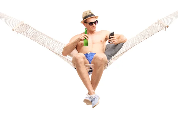 Uomo sdraiato su un'amaca e con in mano una birra — Foto Stock