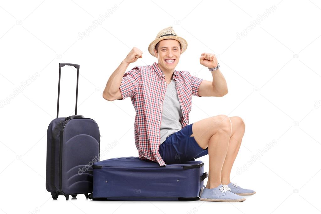 Joyful tourist sitting on his luggage