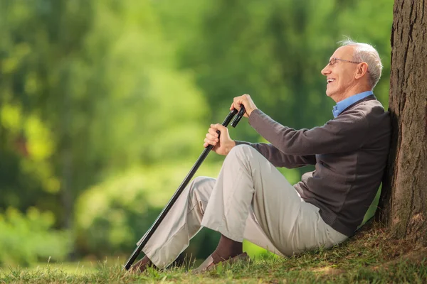 Senior gentleman seated by a tree in a park — Stock Photo, Image