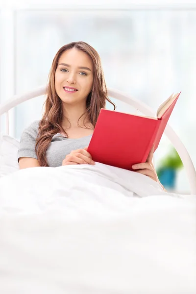 Mulher deitada em uma cama e segurando um livro — Fotografia de Stock