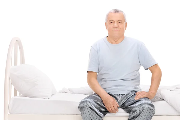 Homme âgé en pyjama assis sur un lit — Photo