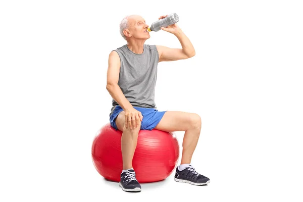 Senior man on fitness ball drinking water — Stock Photo, Image