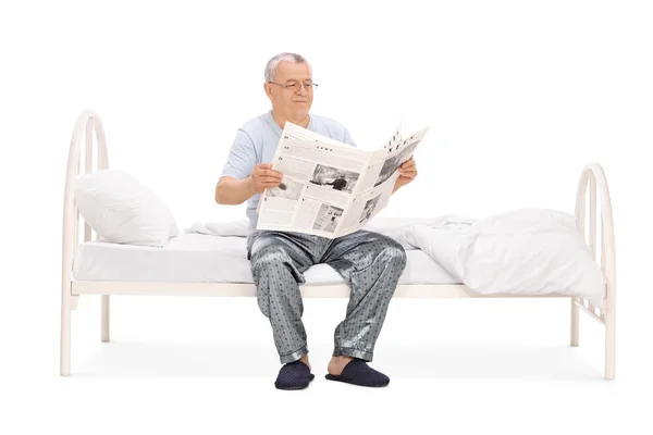 Uomo anziano in pigiama che legge un giornale — Foto Stock