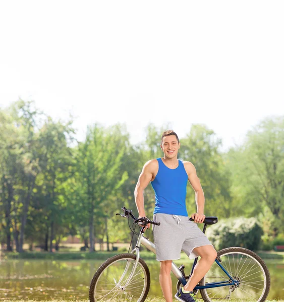 Young cyclist with his bicycle by a pond — Stock Photo, Image