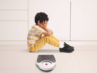 Scared little boy sitting next to a weight scale 