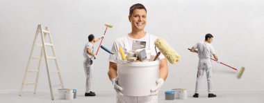 Bir kova alet ve fırçayla duvarı boyayan ressamlardan oluşan bir takım.