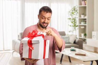 Mutlu genç adam oturma odasında bir hediye açıyor.