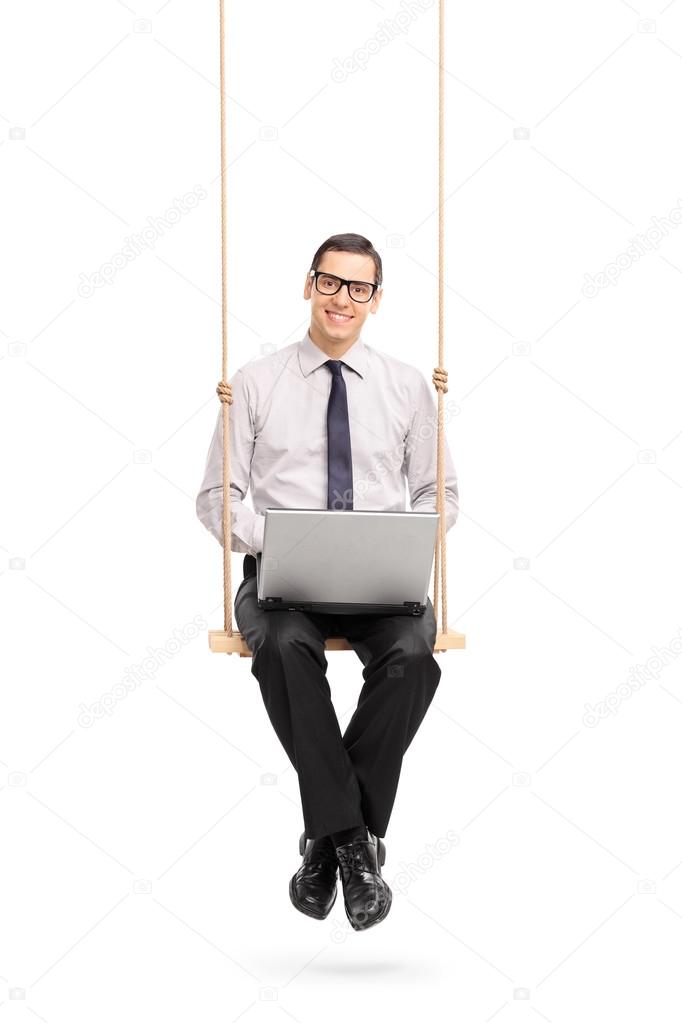 Businessman working on laptop seated on a swing