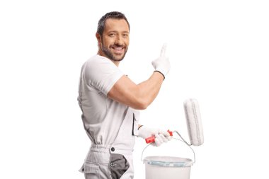 Beyaz boyalı bir kova tutan ve beyaz arkaplanı işaret eden bir ressam.