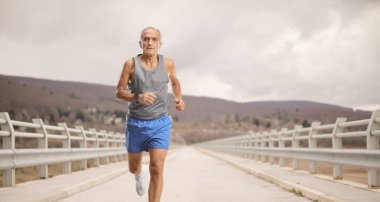 Yaşlı adam bulutlu bir günde köprüde koşuyor.