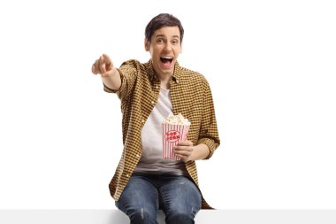 Adam gülüyor, panele işaret ediyor ve beyaz arka planda izole edilmiş patlamış mısır yiyor.