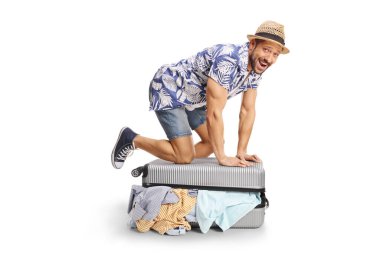 Neşeli bir adam beyaz arka planda izole edilmiş bir bavulu kapatmaya çalışıyor.