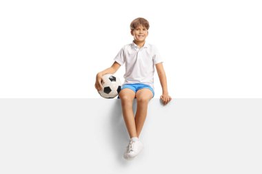 Elinde futbol topu olan mutlu bir çocuk mavi arka planda boş bir panelde oturuyor.