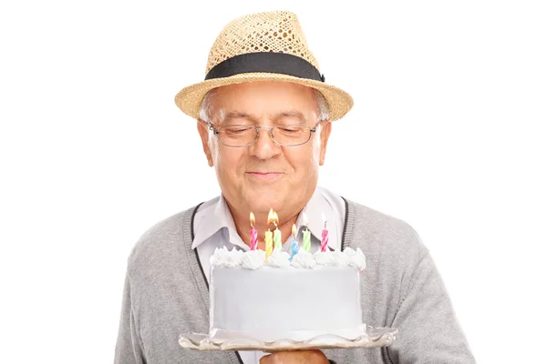 Senior gentleman blowing candles on a birthday cake — 图库照片