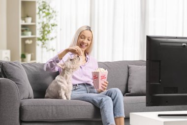 Kanepede köpeğiyle patlamış mısır paylaşan bir kadın.