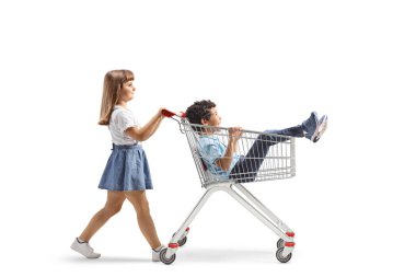 Bir kızın beyaz arka planda izole bir şekilde bir çocuğu alışveriş arabasının içine iterken tam boy profil fotoğrafı.